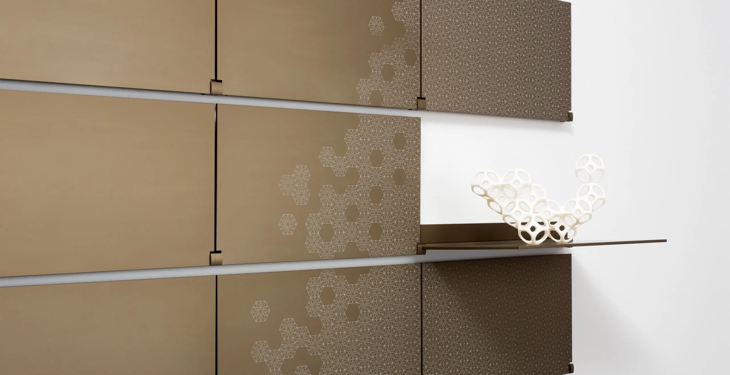 Riveli Luxe Shelves in Aged Bronze with a laser-etched pattern, a shelf folded down with a white sculpture