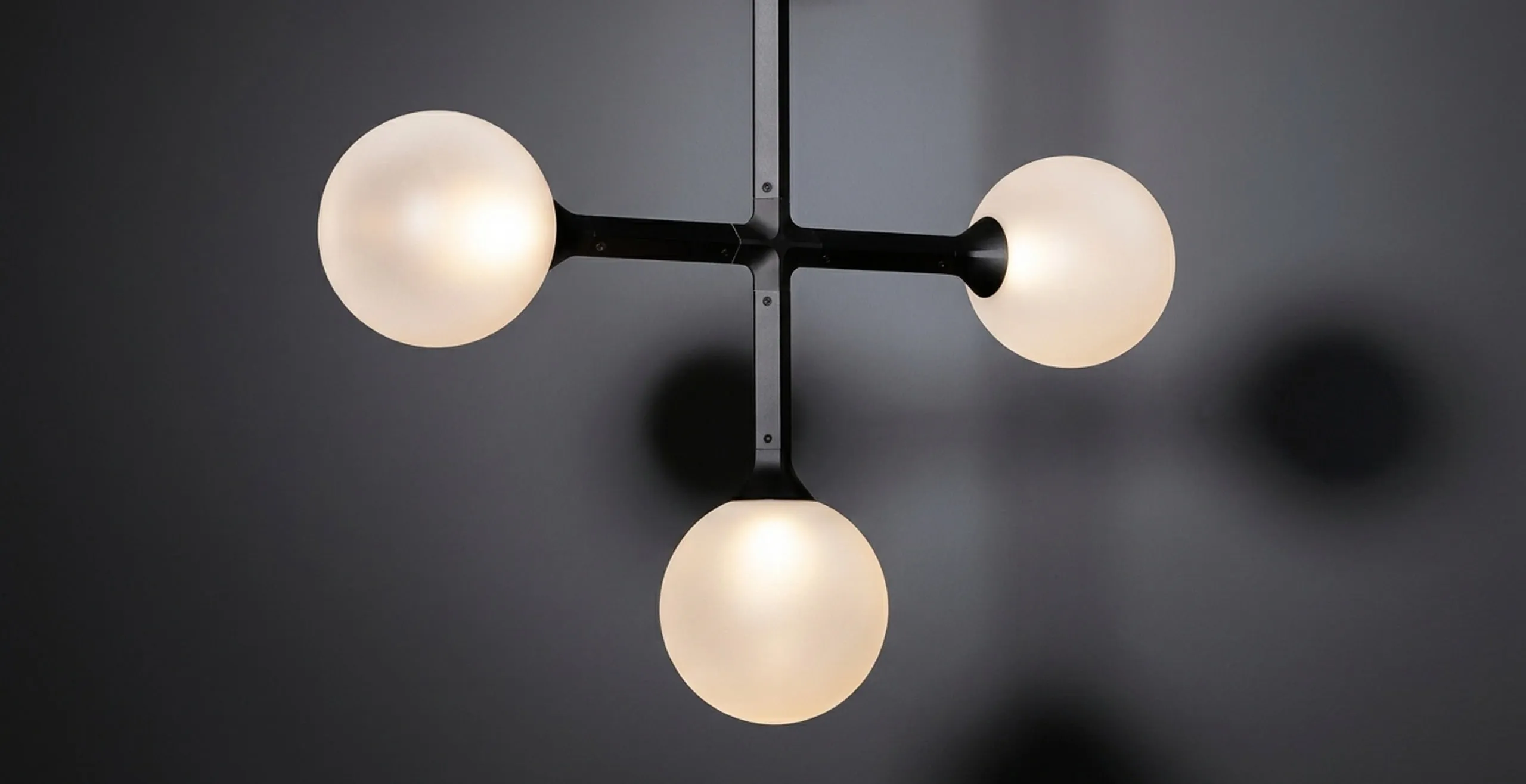 JUNIP globes on a black stem, lit, against a dark wall