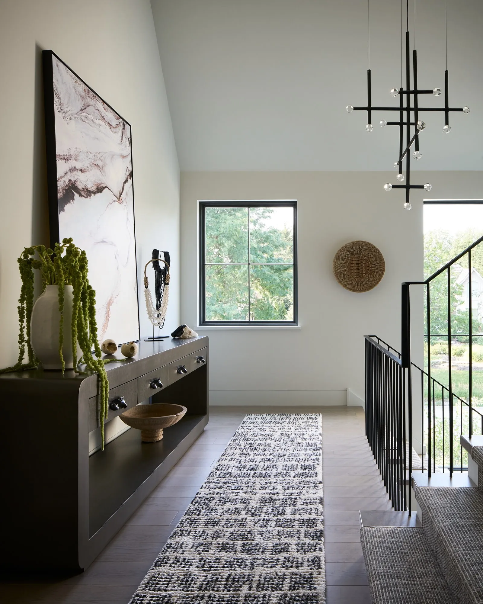 A JOULLE chandelier above the stairwell of a hallway with a long console