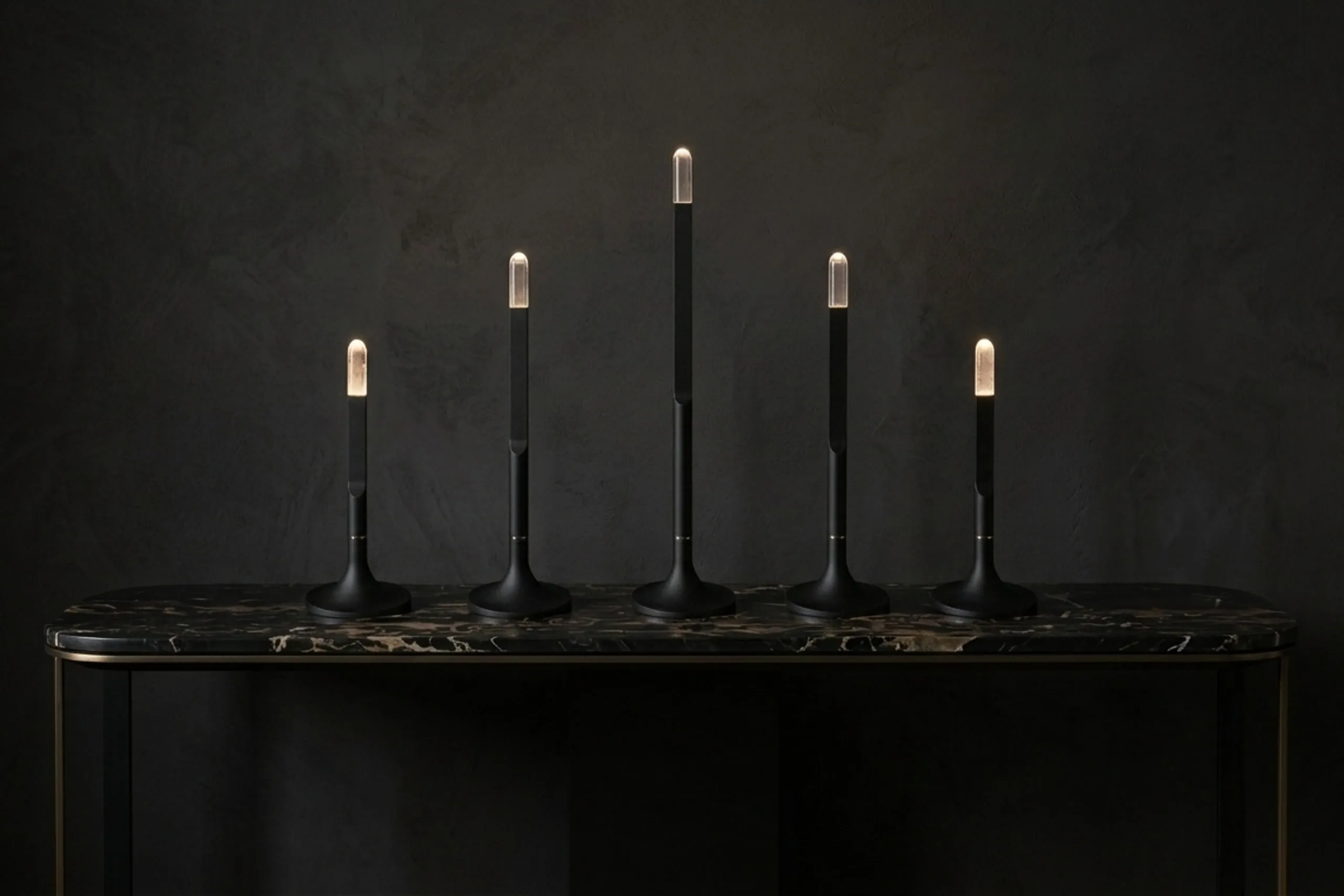 Five Torche lamps in black on a marble console against a dark wall
