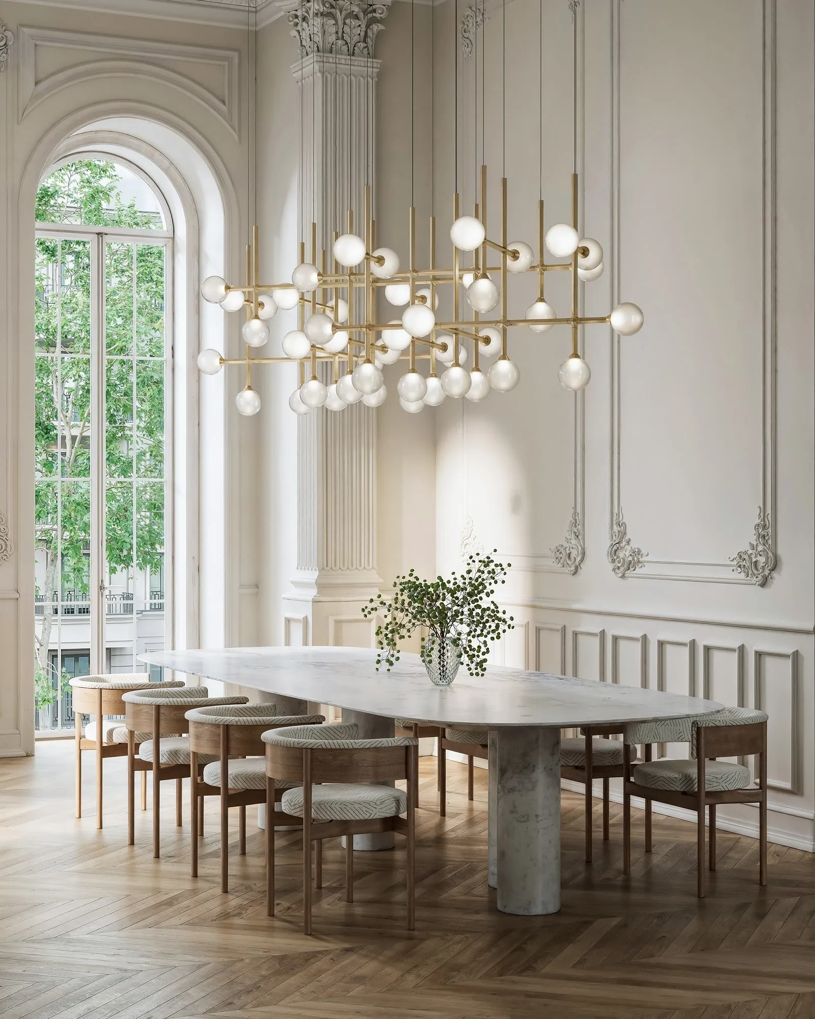JUNIP chandeliers in Satin Brass over a long dining table in a room with tall arched windows