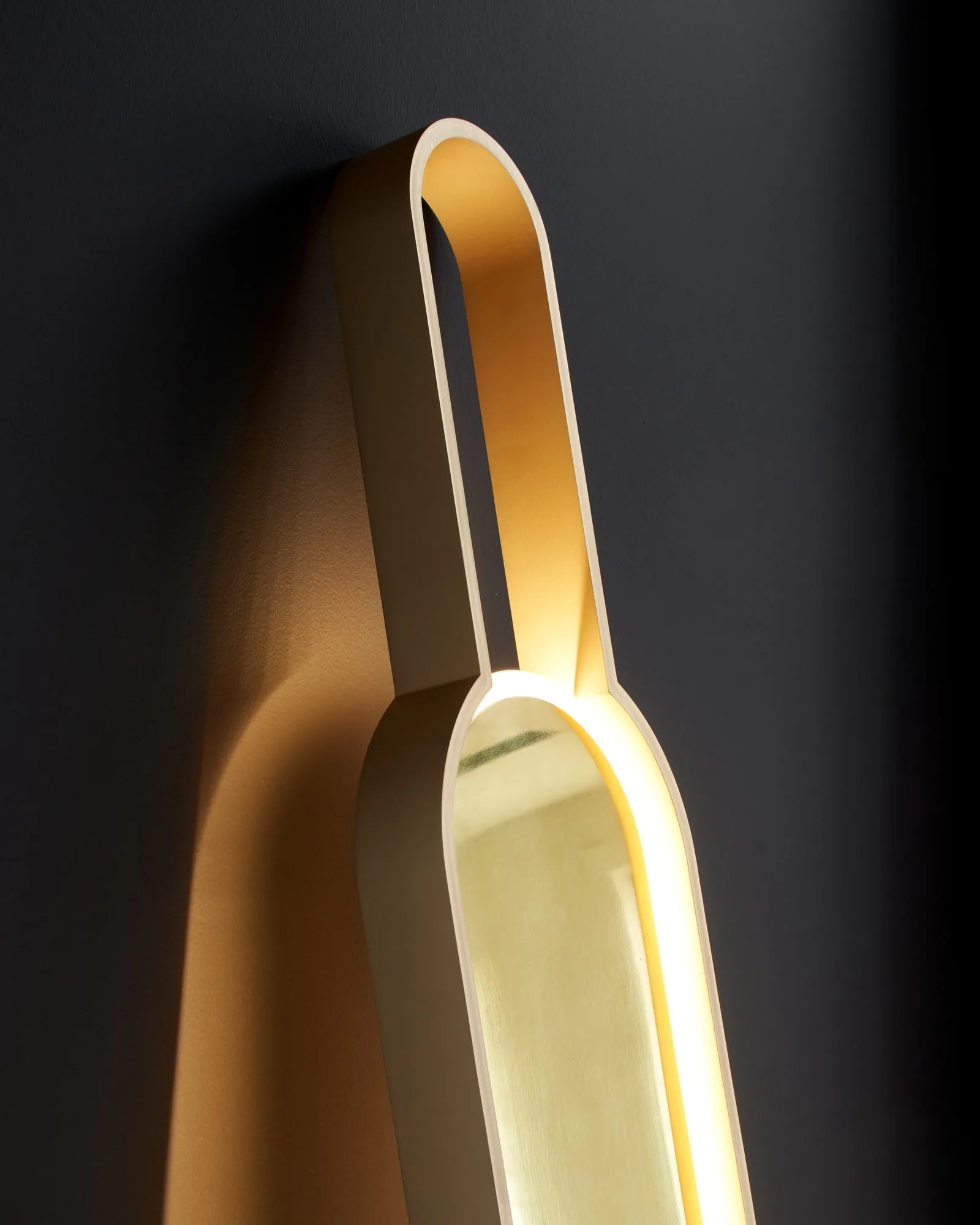 Portal Floor Lamp's brass loop, close up against a dark wall