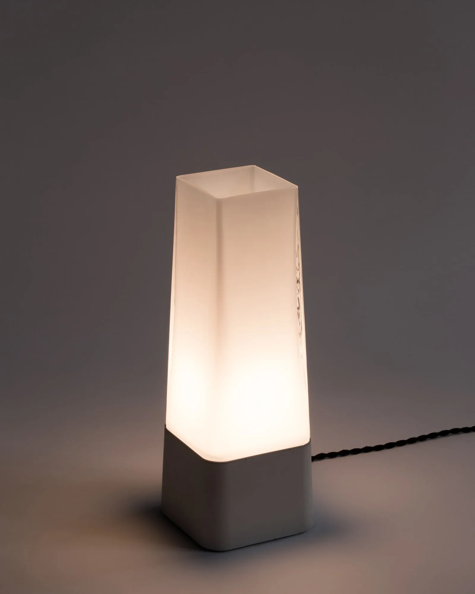 Faaro in white glass, lit, on a grey backdrop