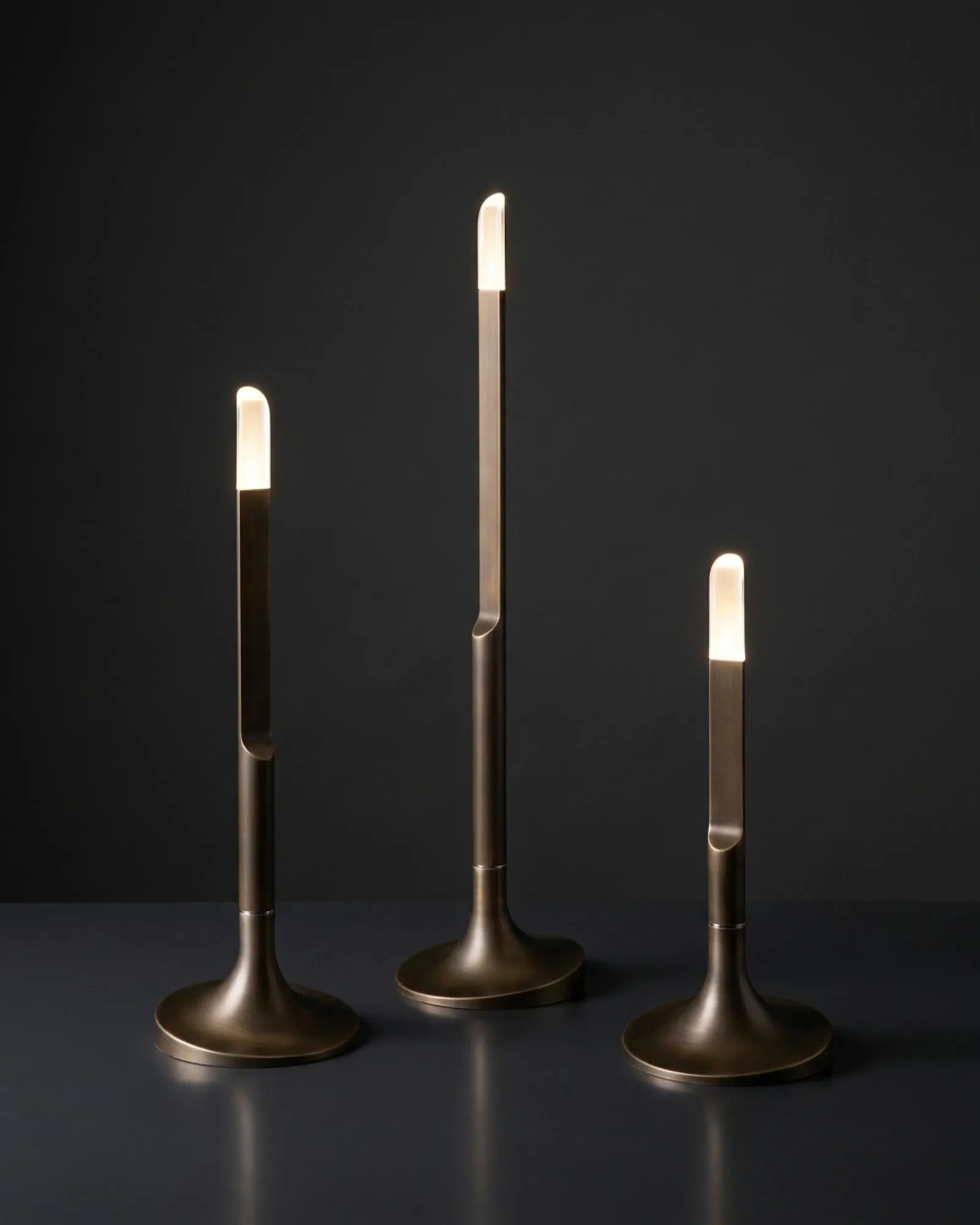 Three Torche lamps in bronze against a dark wall