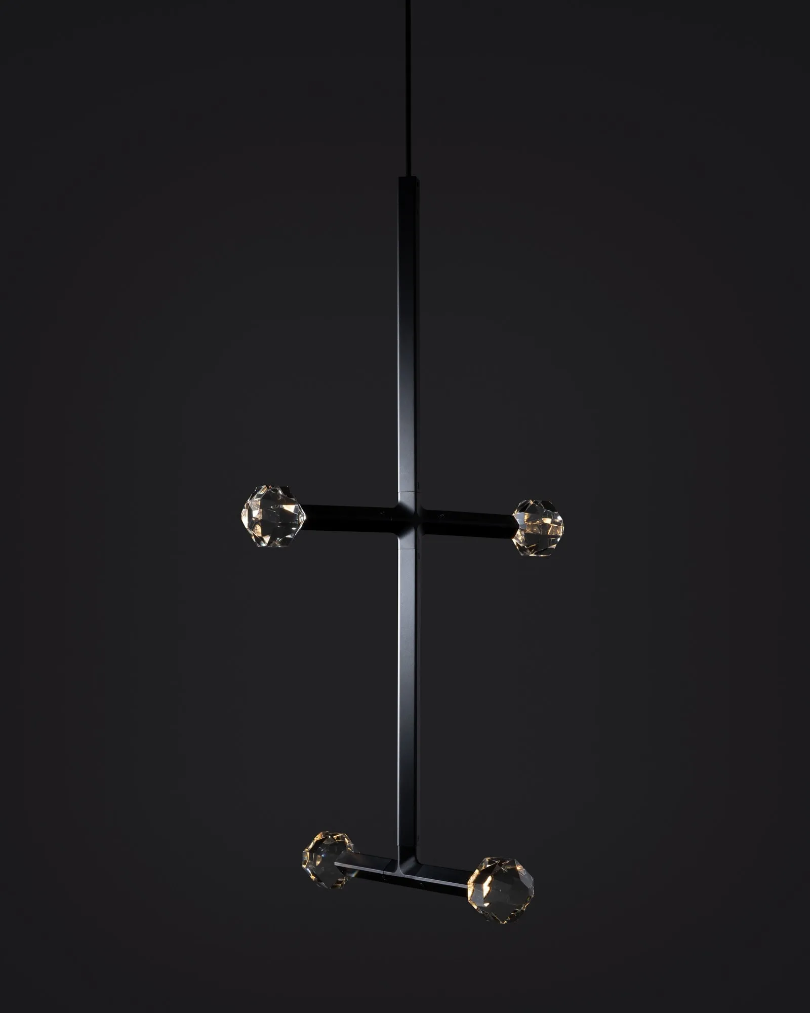 A JOULLE pendant in the studio with two crossbars of crystal stones, against a dark wall