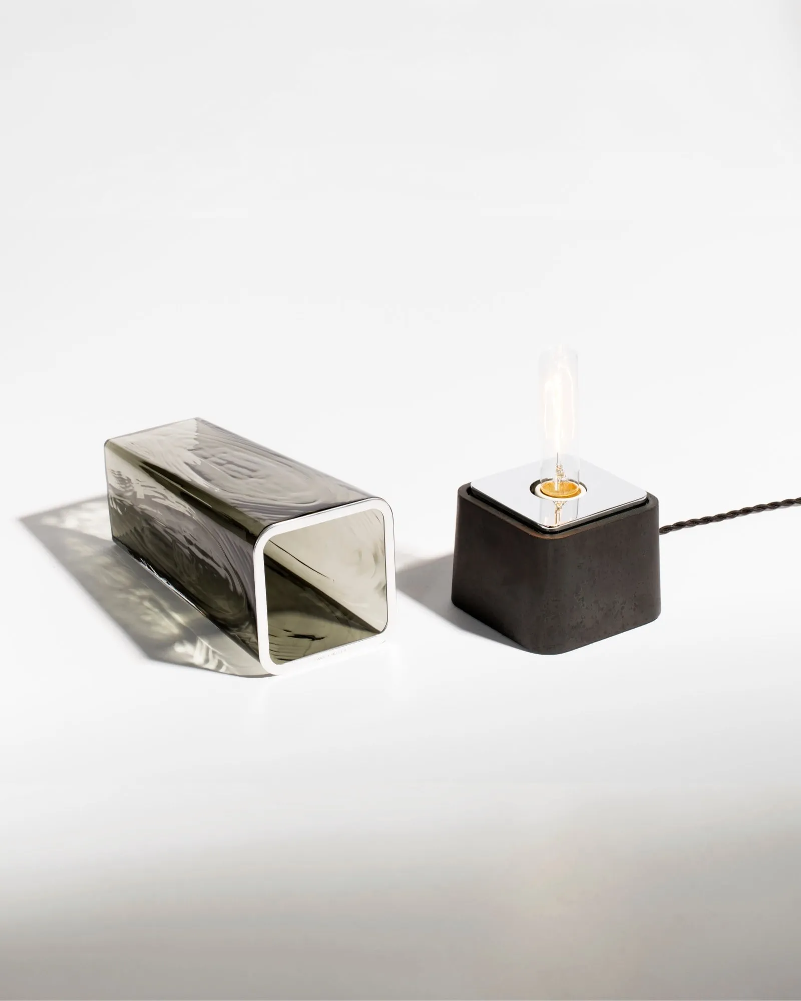 A Faaro glass form in smoke beside its black base, on white
