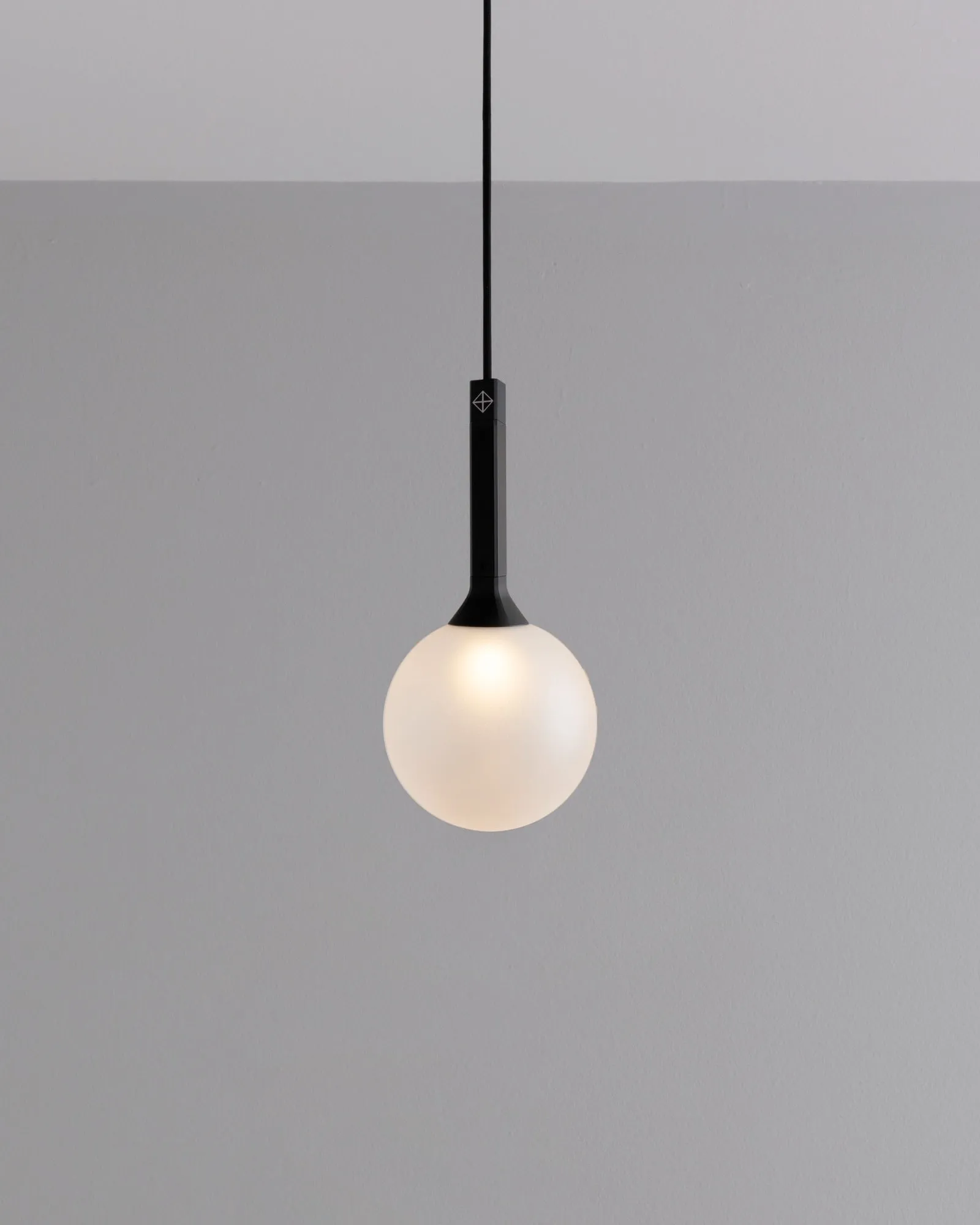 A single JUNIP globe pendant against a grey wall
