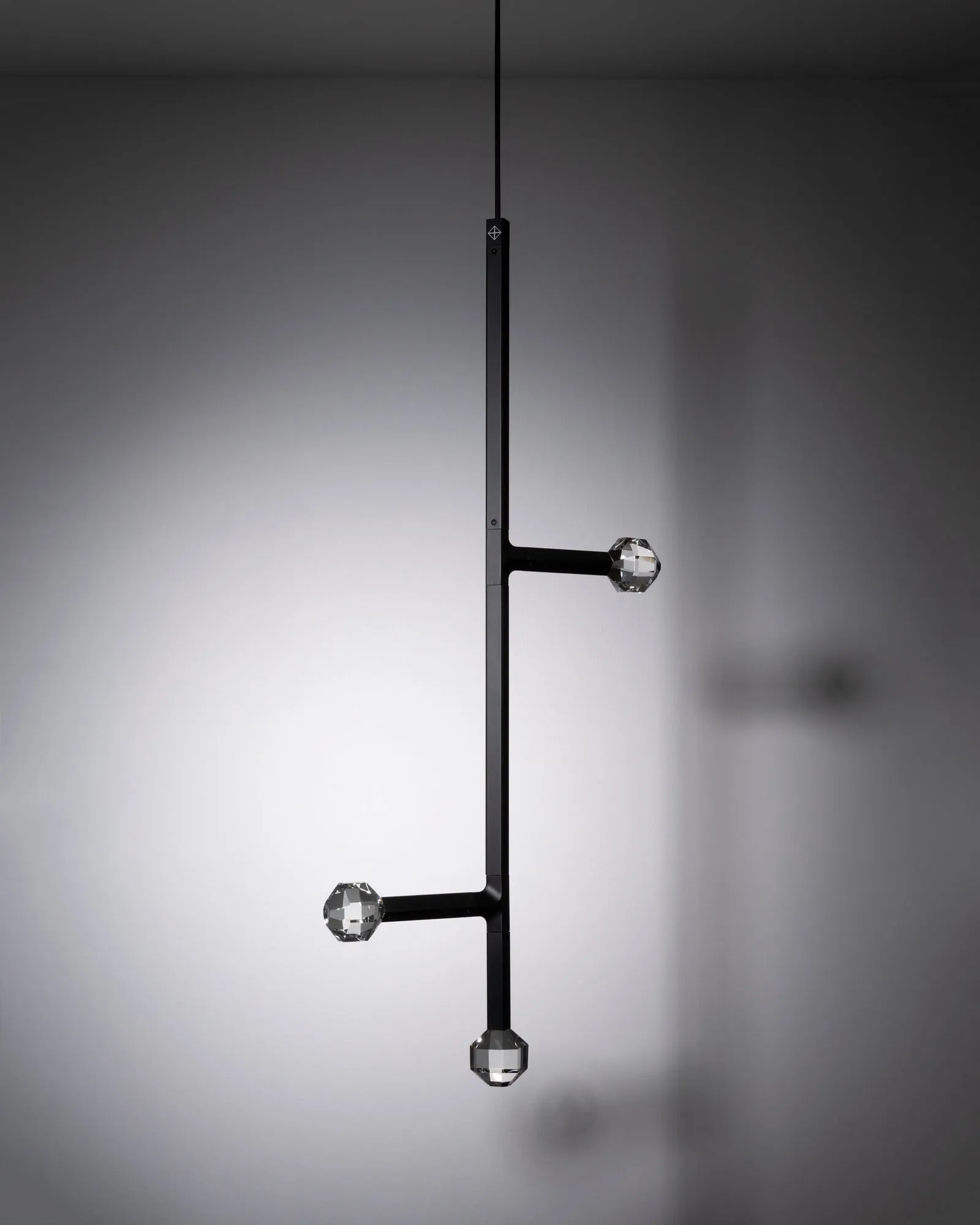 A JOULLE pendant in the studio with two short arms on opposite sides and a crystal stone below