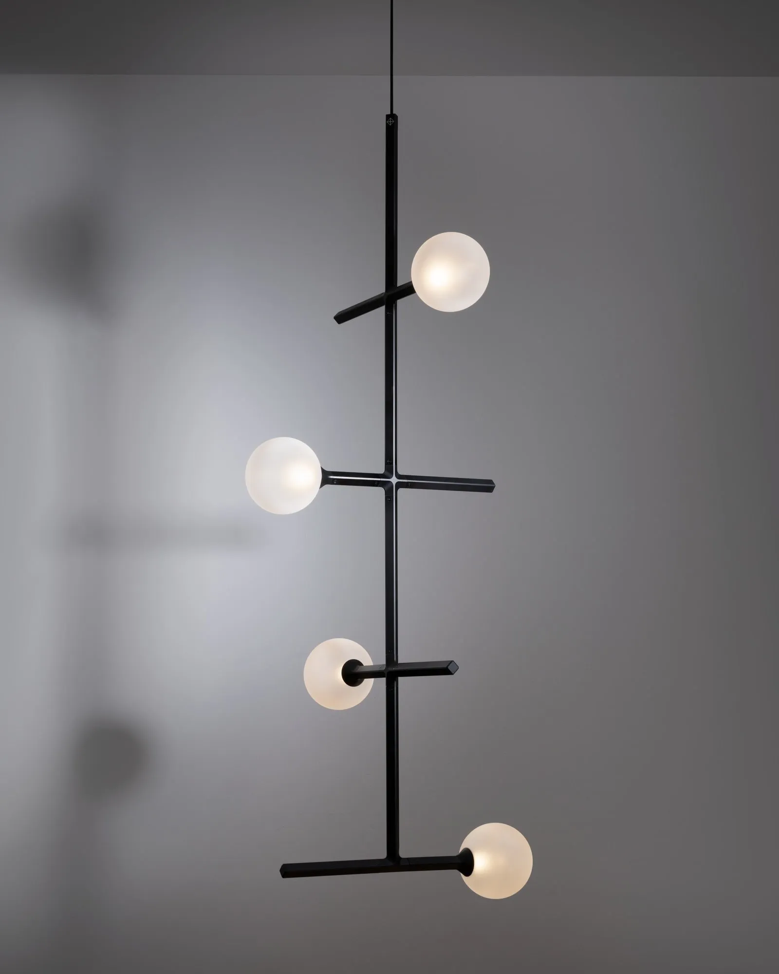 A tall JUNIP pendant with globes on short arms, against a grey wall