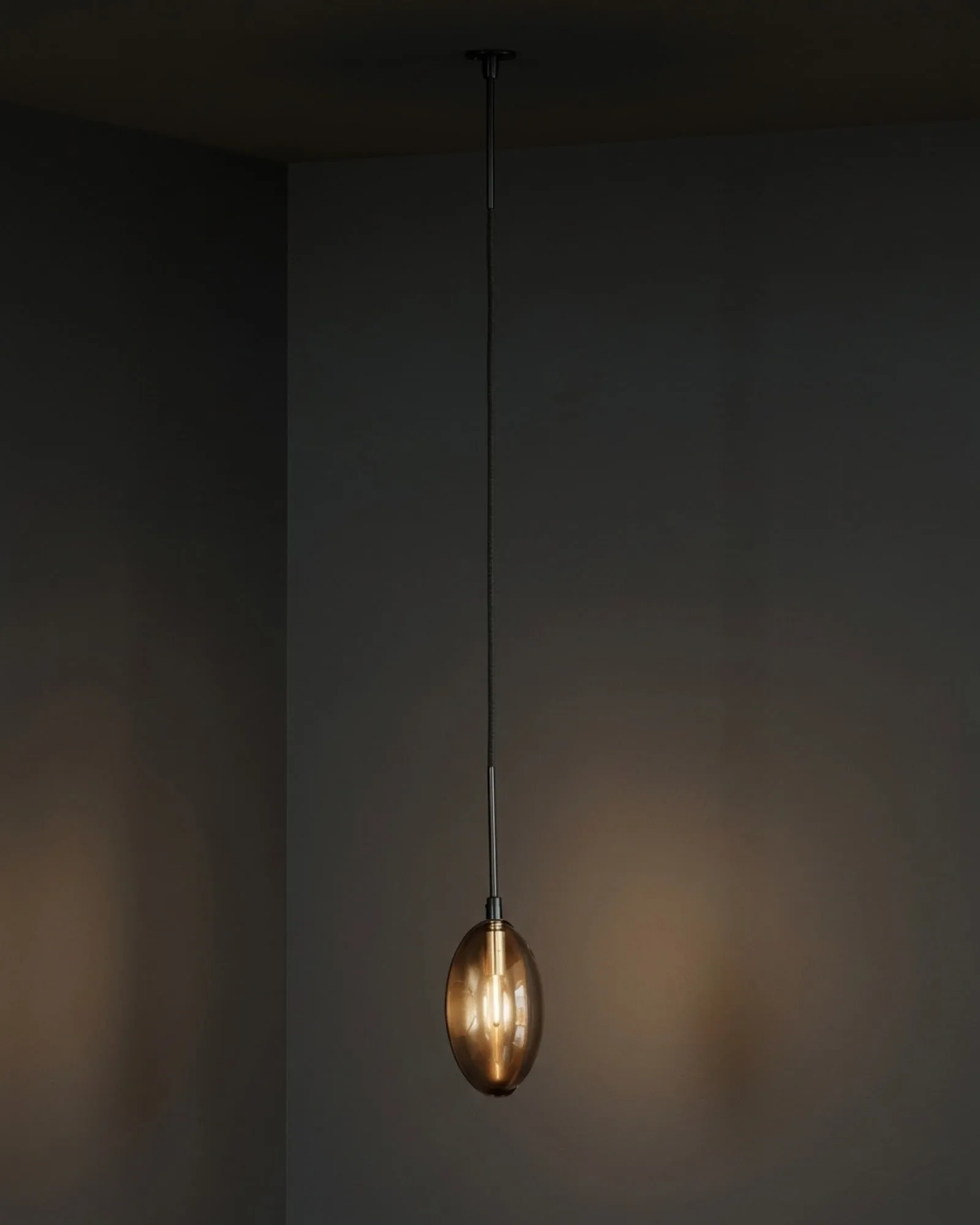 A single Oona pendant in smoke glass in a corner, lit