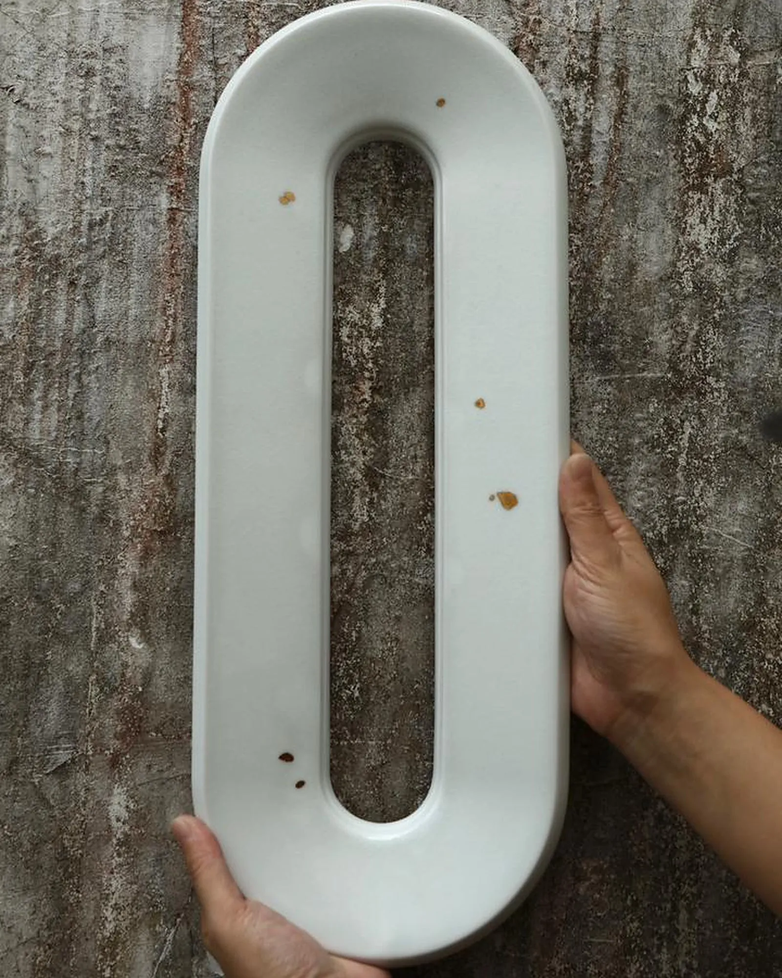 A white Void Ceramic Sconce held against a weathered wall