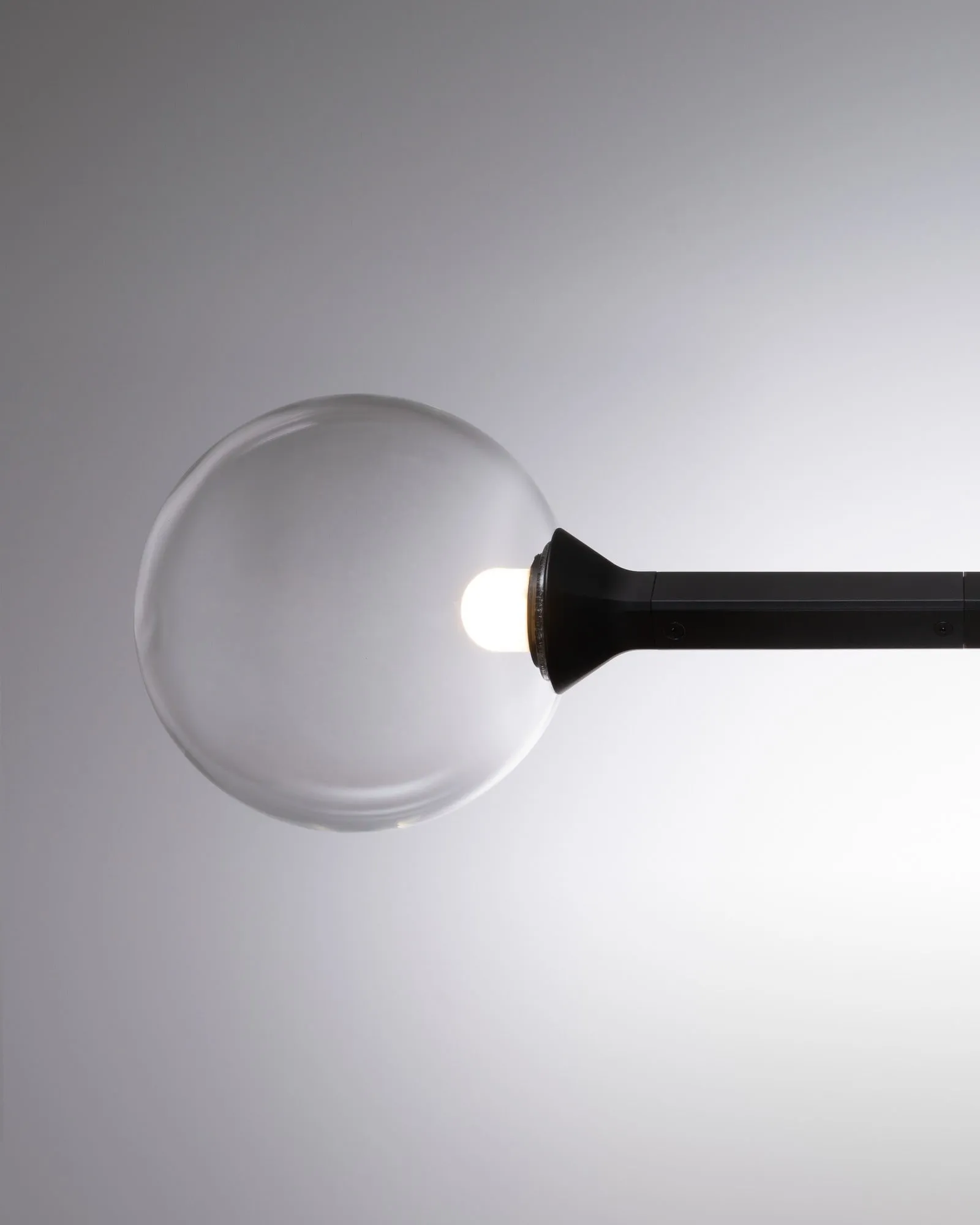 A clear JUNIP glass globe at the end of an arm, close up