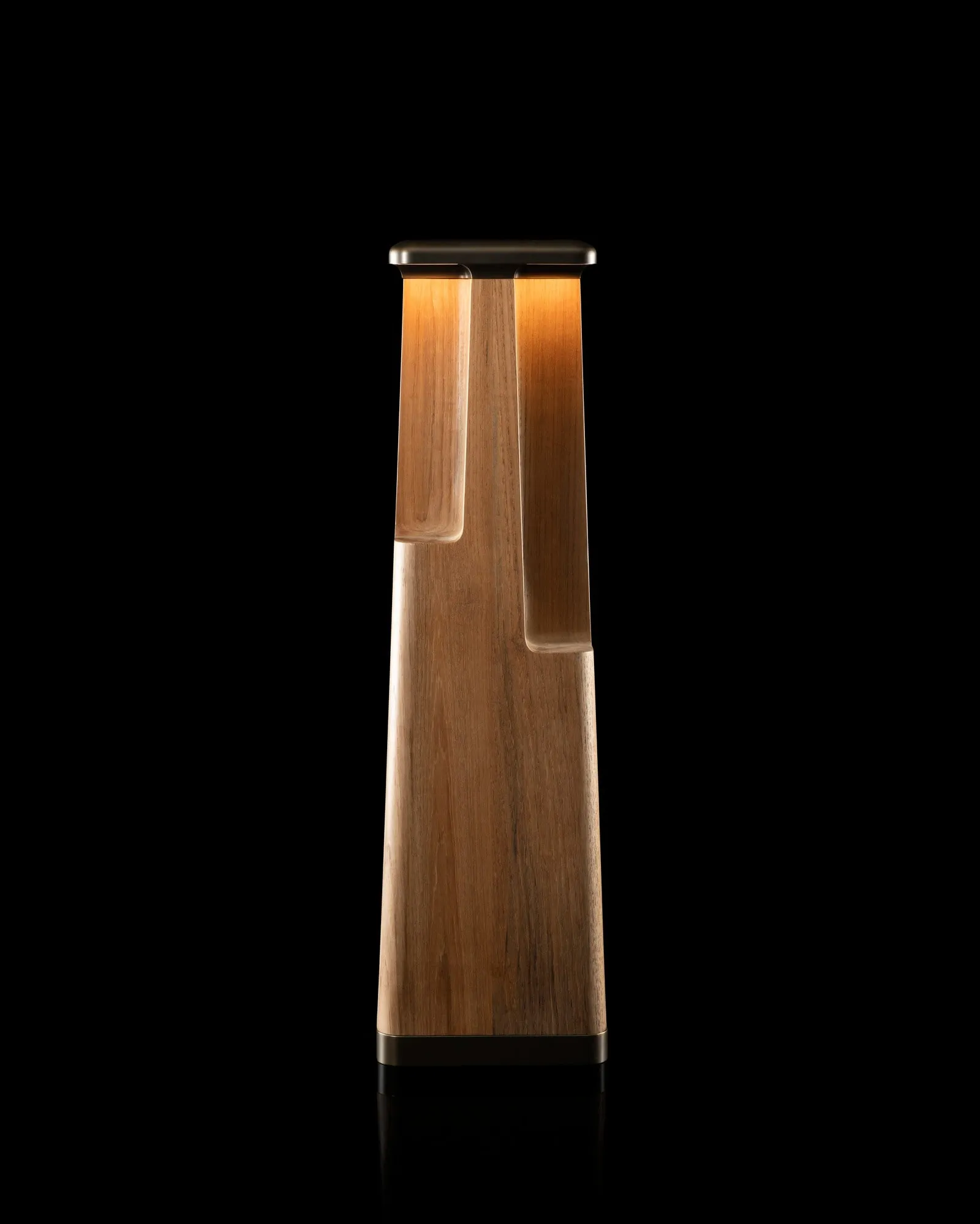 A Totem Floor Lamp in teak, lit, against black
