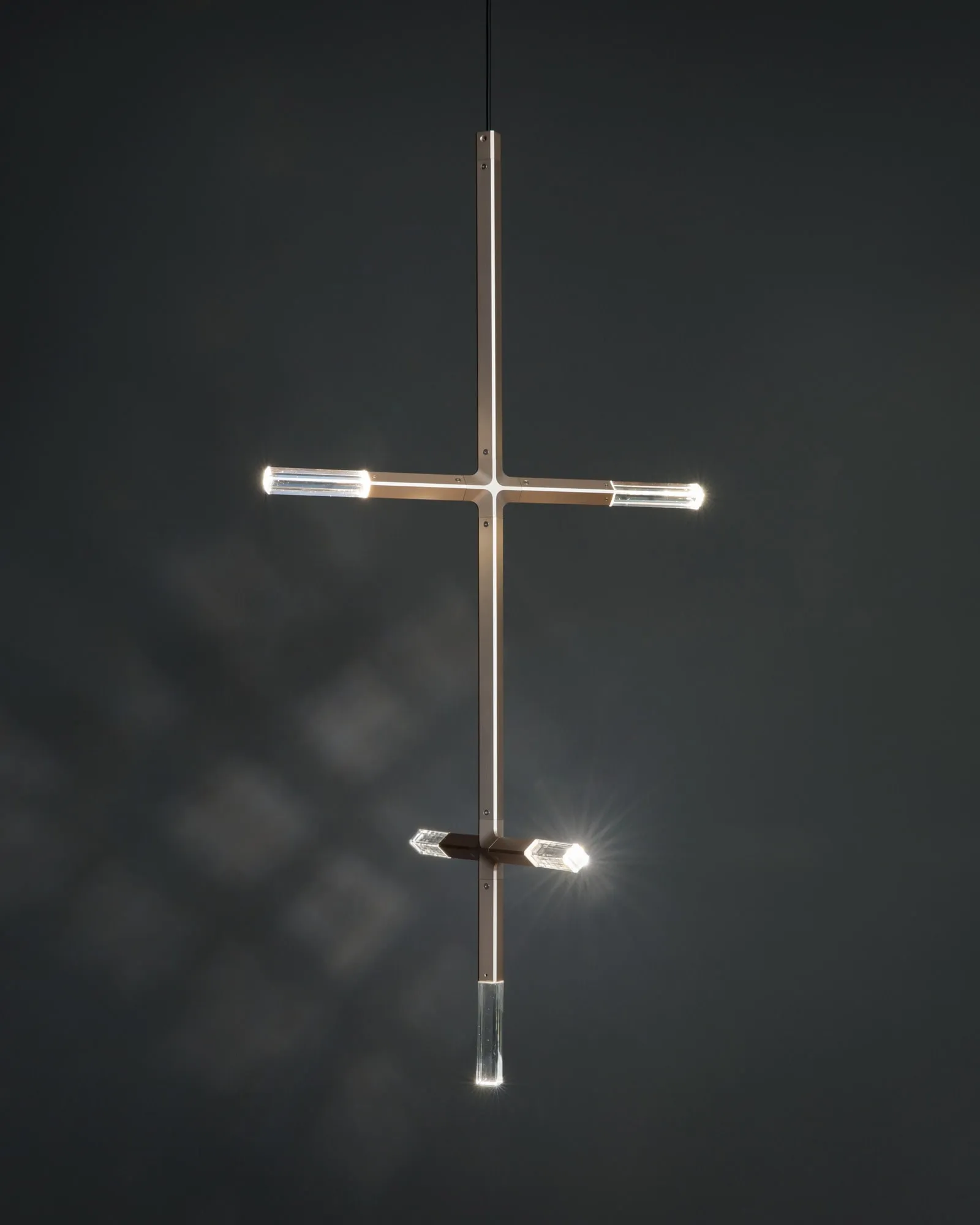 A JAX pendant in Satin Brass glowing against a dark wall