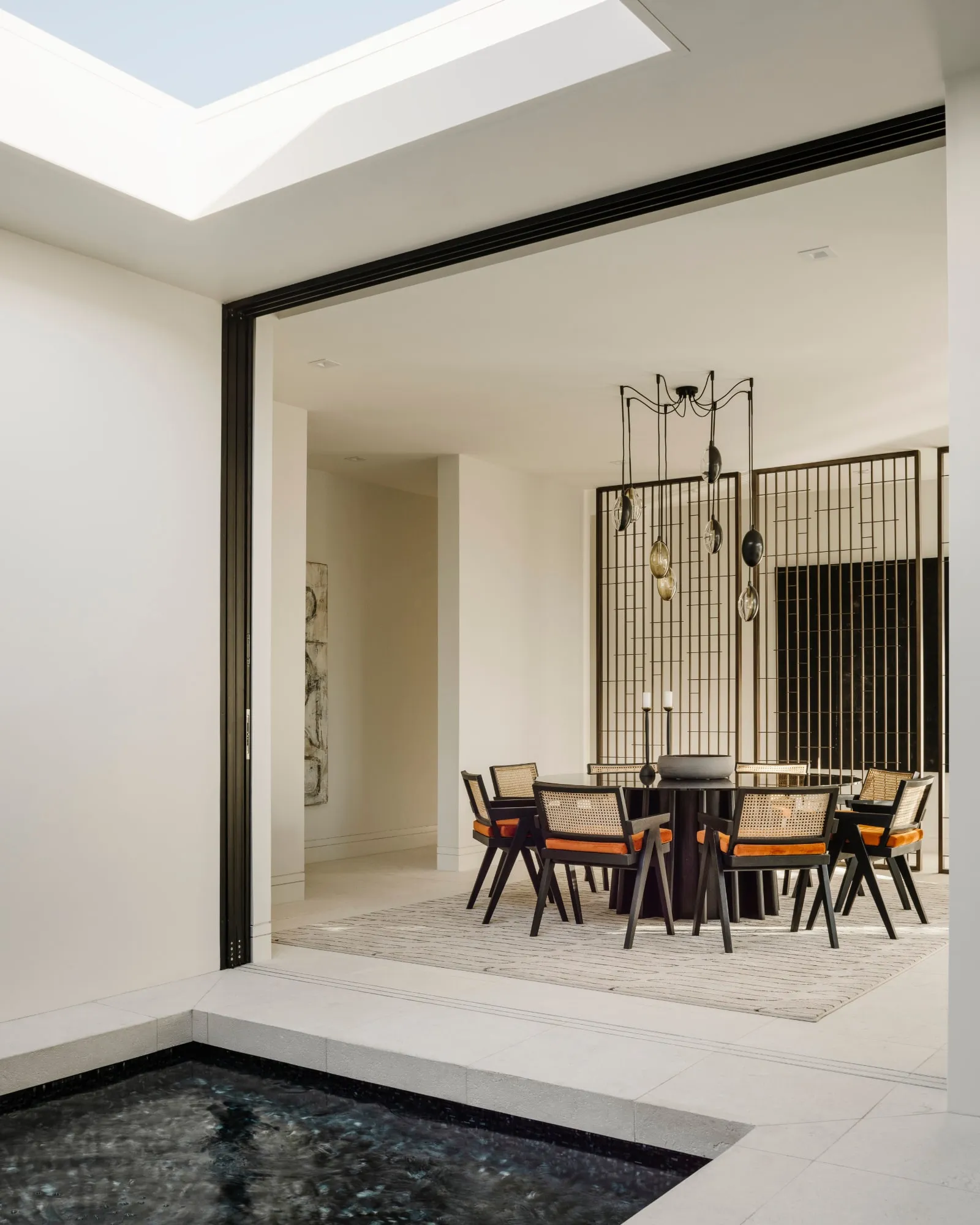 An Oona chandelier over a round dining table, seen across an indoor courtyard pool