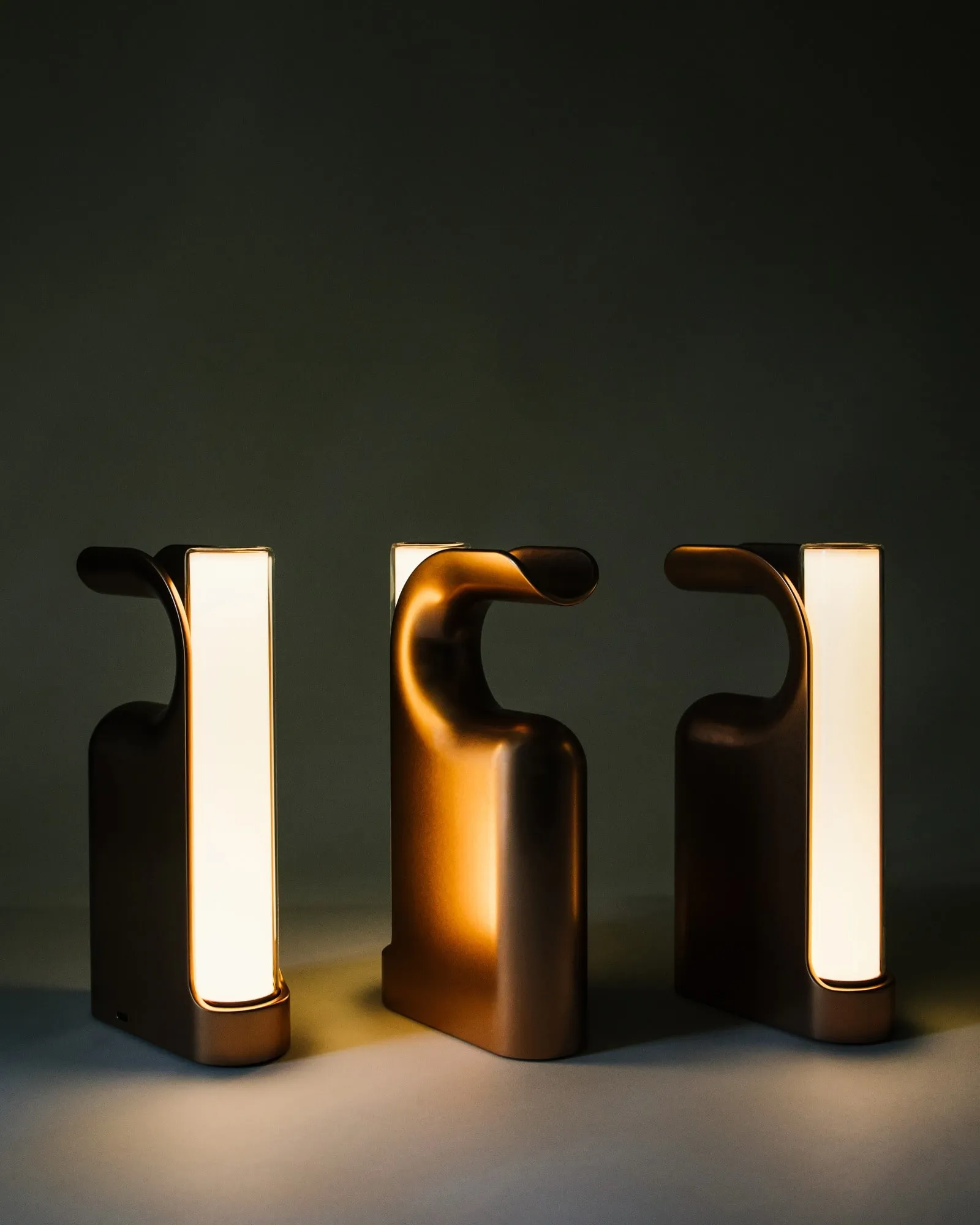 Three Fable Lanterns in bronze, lit, against a dark wall