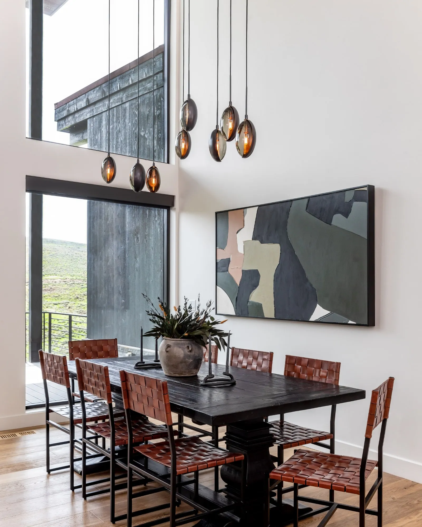 Oona pendants at staggered heights over a dining table beside an abstract painting